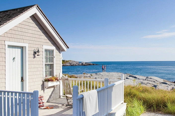 Charming shore cottage porch with a draped white towel, rocking chair, and sweeping ocean view on a clear summer day