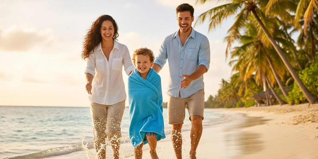 Parents and child laughing on a sandy beach at sunset, boy bundled in a bright blue rental beach towel